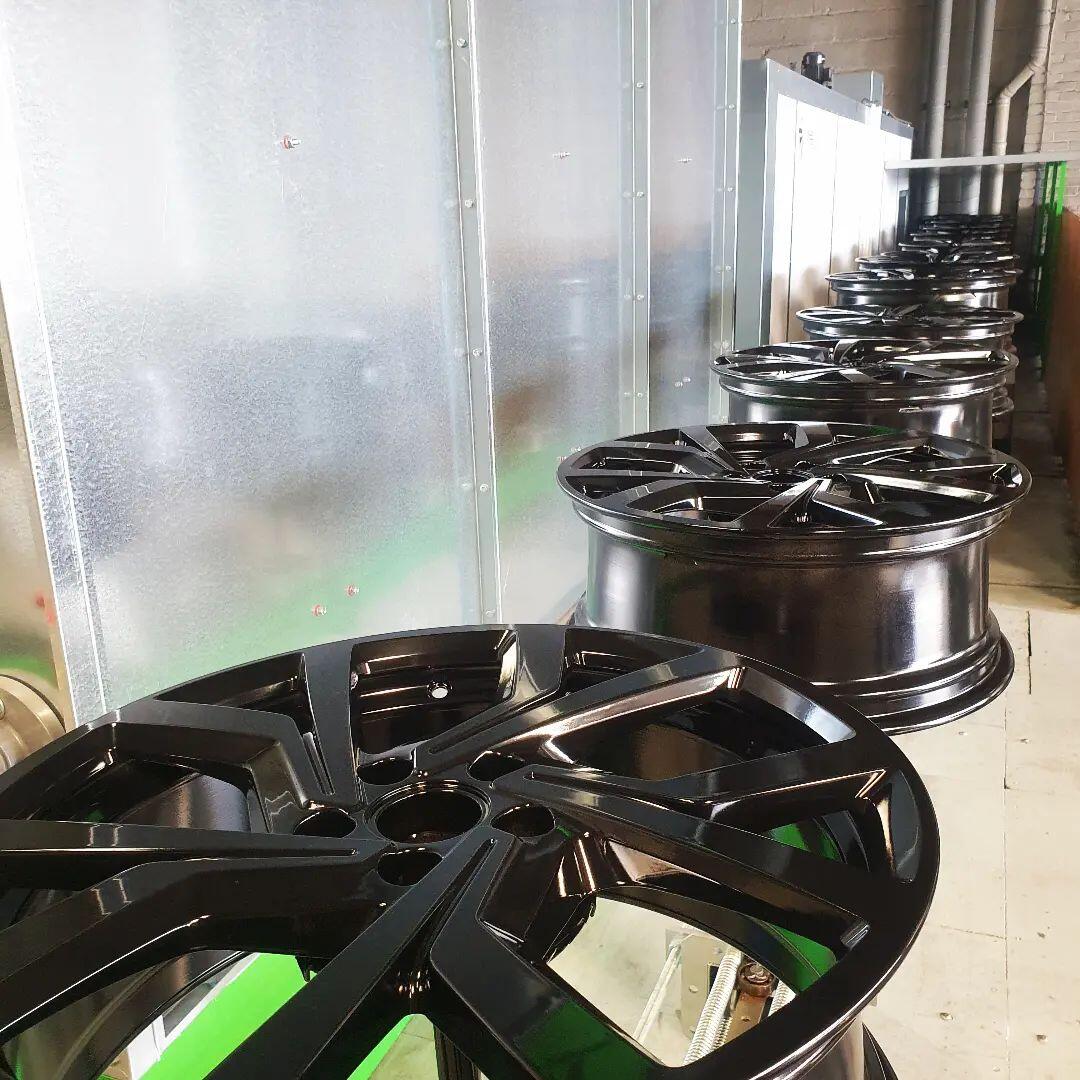 Stack of gloss black refurbished alloy wheels ready for fitting